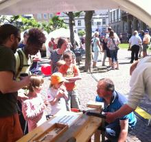 Das TEam der Holzwerkstatt beim Austesten der Belastbarkeit von Furnierholz vor den Augen neugieriger Kinder